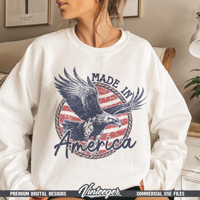 May include: White sweatshirt featuring a graphic of an eagle with outstretched wings, set against a red and white striped background. The text "MADE IN America" is displayed in a circular design. The sweatshirt has a crew neck.