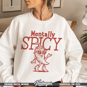 May include: White sweatshirt with the text "Mentally Spicy" in red. A cartoon chili pepper wearing sunglasses and boots is featured below the text. The sweatshirt has a crew neck and long sleeves.
