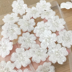 May include: White floral appliques with sequins and beads on a sheer mesh fabric. The appliques are perfect for adding a touch of elegance to any project.