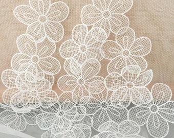 May include: A collection of white lace flower appliques featuring a delicate grid-like mesh pattern within each petal. These individual floral motifs are arranged in a cluster, showcasing intricate thread work and openwork detailing throughout.