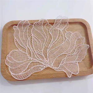 May include: A delicate, off-white lace applique featuring an intricate, flowing floral pattern with scalloped edges. The design is composed of fine, interconnected mesh threads that form organic, petal-like shapes, creating a lightweight, semi-sheer textile piece.
