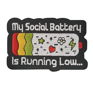 Puede incluir: Parche bordado con el texto "My Social Battery Is Running Low...". El parche presenta un gráfico de batería con secciones rojas, amarillas y verdes, junto con elementos decorativos como estrellas, un corazón, una flor y un rayo.