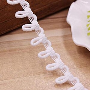 May include: A white loop trim featuring a continuous row of small, uniform fabric loops attached to a narrow woven tape. The trim is constructed from a soft, textured material and is designed for decorative edging or functional button closures.