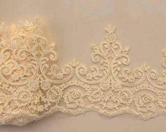 May include: A cream-colored lace trim featuring an intricate embroidered pattern of swirling floral motifs and rose blossoms. The decorative border has a scalloped edge with detailed stitching, showcasing a dense, textured design throughout.