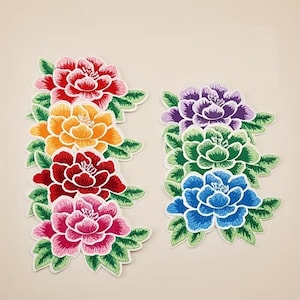 May include: A collection of seven embroidered flower patches featuring layered petals in shades of red, orange, dark red, pink, purple, green, and blue, each surrounded by green leaves with white outlines on a plain light background.