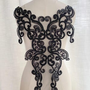 May include: Black beaded lace applique with a floral design. The lace is delicate and intricate, with a lot of detail. It would be perfect for adding a touch of elegance to a garment or project.