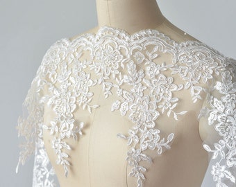 May include: White lace trim with a floral design. The lace is delicate and intricate, with a scalloped edge. It would be perfect for adding a touch of elegance to a wedding dress, bridal gown, or other special occasion garment.