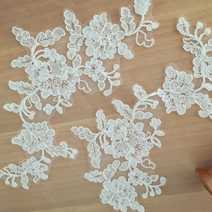 May include: White lace appliques with floral designs. The appliques are delicate and intricate, with a variety of flower shapes and sizes. They would be perfect for adding a touch of elegance to a wedding dress, bridal accessories, or other craft projects.