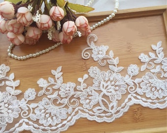 May include: White lace trim with a floral design. The lace has a scalloped edge and is decorated with small beads.