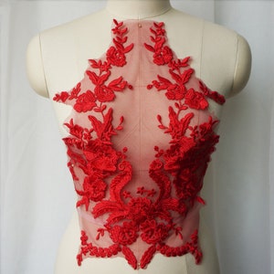 May include: A red floral lace applique with intricate embroidered details. The applique features a variety of flowers and leaves, creating a delicate and ornate design. The lace is attached to a sheer, light pink backing, perfect for embellishing garments.