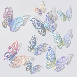 May include: A collection of iridescent butterfly decorations in various sizes. The butterflies have intricate cut-out patterns and are in shades of pink, blue, green, and yellow. They appear to be floating against a soft, white background.