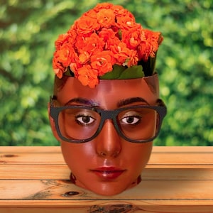 May include: A person's face with orange flowers growing out of the top of their head. The person is wearing black framed glasses.