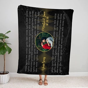 May include: Black and gold personalized blanket with a couple's photo and the text "Your Song" and "Martin & Jane 10.20.18". The blanket is decorated with musical notes.