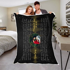 May include: Black and white personalized blanket with a photo of a couple and the text "Your Song", "Martin & Jane", and "10.20.18". The blanket has a musical note design and the text "Write lyrics here" repeated throughout.