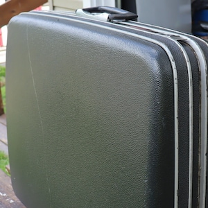 May include: A dark green hard-sided suitcase with silver trim. The suitcase has a handle on the top and is closed.