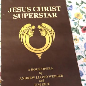 May include: A brown vintage album cover for "Jesus Christ Superstar," a rock opera by Andrew Lloyd Webber and Tim Rice, released in October 1970. The cover features gold lettering and a stylized emblem.