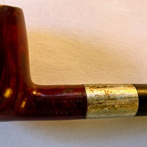 May include: A brown wooden pipe with a silver band and a black mouthpiece.