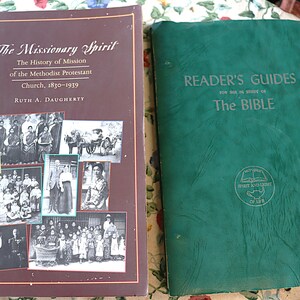 May include: A brown book titled The Missionary Spirit The History of Mission of the Methodist Protestant Church 1830-1939 by Ruth A. Daugherty with black and white historical photos, next to a green book titled Reader's Guides for the Study of The Bible.