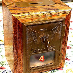 May include: A wooden bank with a slot on top and a metal front. The front features an eagle emblem, a key, and the number 4. The bank has a natural wood grain finish and brass accents.