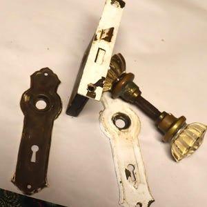 May include: Antique brass door hardware set with a white porcelain knob and backplate. The set includes a door handle, a keyhole cover, and a strike plate.