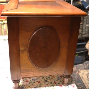 May include: A wooden antique box with a rectangular top and an oval-shaped design on the side. The box is made of a warm-toned wood and has four rounded legs. The box appears to be well-preserved and has a classic design.