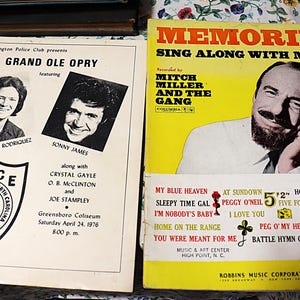 May include: Two vintage music memorabilia items. One is a yellow album cover titled "Memories Sing Along With Mitch" featuring Mitch Miller. The other is a black and white flyer for a Grand Ole Opry show.