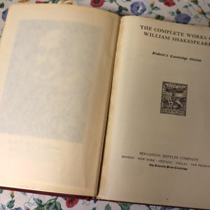 May include: An open book with off-white pages, featuring the title "THE COMPLETE WORKS OF WILLIAM SHAKESPEARE" in black text. The book is a Student's Cambridge Edition, published by Houghton Mifflin Company. A small illustration is also visible.