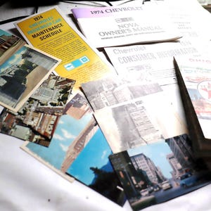 May include: A collection of vintage postcards and car manuals, including a 1974 Chevrolet Nova Owner's Manual, a 1974 Chevrolet Consumer Information booklet, and a Texaco gas station map. The postcards feature images of buildings and landscapes.