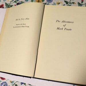 May include: An open book with cream-colored pages. The left page displays the text "Books by Jerry Allen", followed by "Hearth in the Snow" and "The Adventures of Mark Twain". The right page reads "The Adventures of Mark Twain".