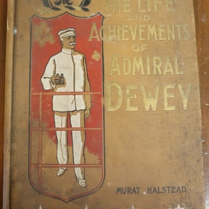 May include: A vintage book cover with a gold background and a red and gold shield. The shield features a portrait of a man in a white uniform and a captain's hat. The text on the cover reads "The Life and Achievements of Admiral Dewey" and "MVRAT HALSTEAD".