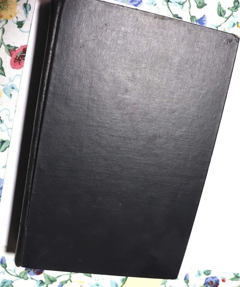 May include: A black hardcover book with a textured cover. The book is slightly angled, revealing a white edge and a floral patterned background.