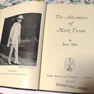 May include: An open book featuring a black and white photograph of Mark Twain and the title "The Adventures of Mark Twain" by Jerry Allen. The book is from the Bloomer Public Library.