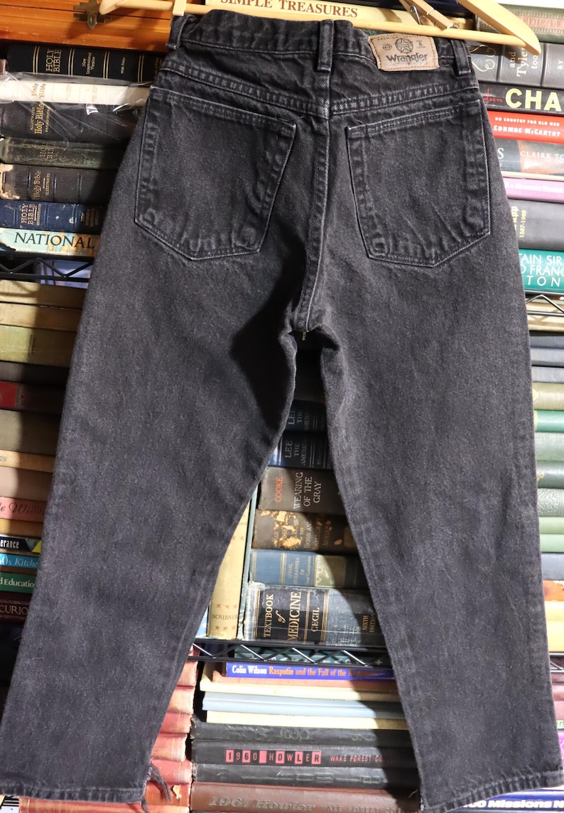 May include: Black denim jeans with a Wrangler label on the back pocket. The jeans have a high waist and a straight leg.