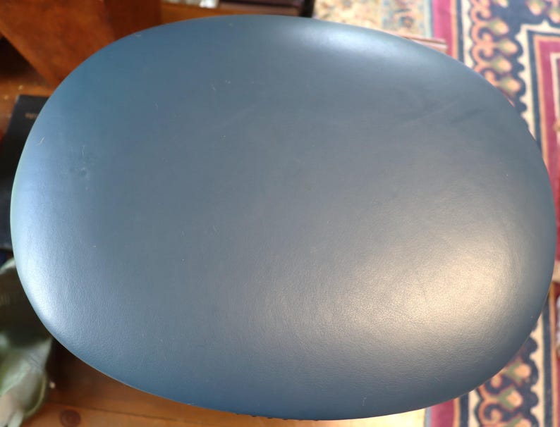 Op de afbeelding: Een effen, ovaalvormig object in blauwgrijs. Het oppervlak vertoont subtiele tintvariaties. Het object is waarschijnlijk gemaakt van een massief materiaal, mogelijk hout of een composiet. De vorm suggereert dat het een tafelblad of een decoratief element kan zijn.