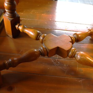 Op de afbeelding: Close-up van de onderkant van een houten tafel. De tafel heeft vier poten, elk met een vierkante basis en een gedraaid, decoratief ontwerp. De poten zijn verbonden door een centrale houten steun.