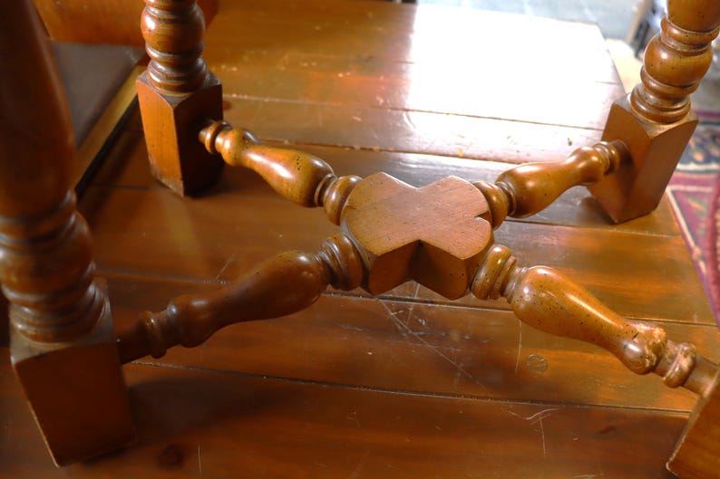 Op de afbeelding: Close-up van de onderkant van een houten tafel. De tafel heeft vier poten, elk met een vierkante basis en een gedraaid, decoratief ontwerp. De poten zijn verbonden door een centrale houten steun.