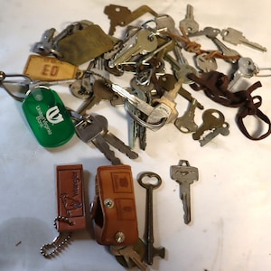 Over a pound of vintage keys including a vintage mustang key a skeleton key a oldsmobile key cover and a wrangler keychain.