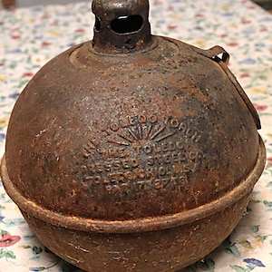 May include: A spherical, rusted metal Toledo Torch with a top vent and a handle attachment. The embossed text reads: THE TOLEDO TORCH, THE TOLEDO PRESSED STEEL CO., TOLEDO OHIO U.S.A., PAT 7-27-26. The surface is heavily oxidized with a dark brown patina.