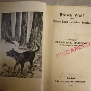 May include: A vintage book titled "Brown Wolf and Other Jack London Stories" with a black and white illustration of a wolf in a forest on the cover. The book is marked "Discarded" by a red stamp.