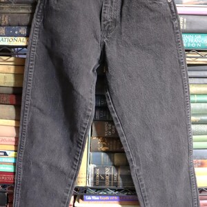 May include: Black denim jeans with a straight leg and a frayed hem. The jeans have a classic five-pocket style and a button fly.