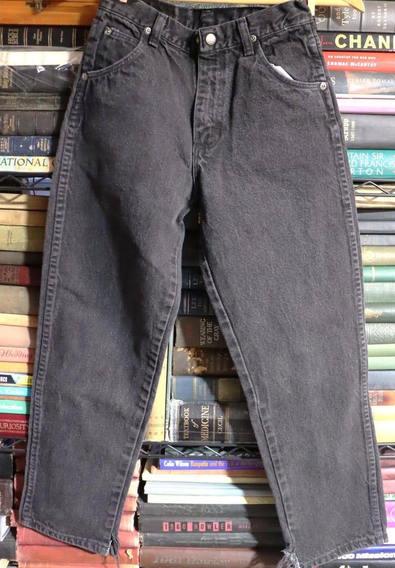 May include: Black denim jeans with a straight leg and a frayed hem. The jeans have a classic five-pocket style and a button fly.