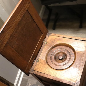 May include: A vintage wooden box with a hinged lid, open to reveal a circular, tiered interior. The box is made of a warm-toned wood, with visible grain and brass hinges. The lid is open, showing the interior design.