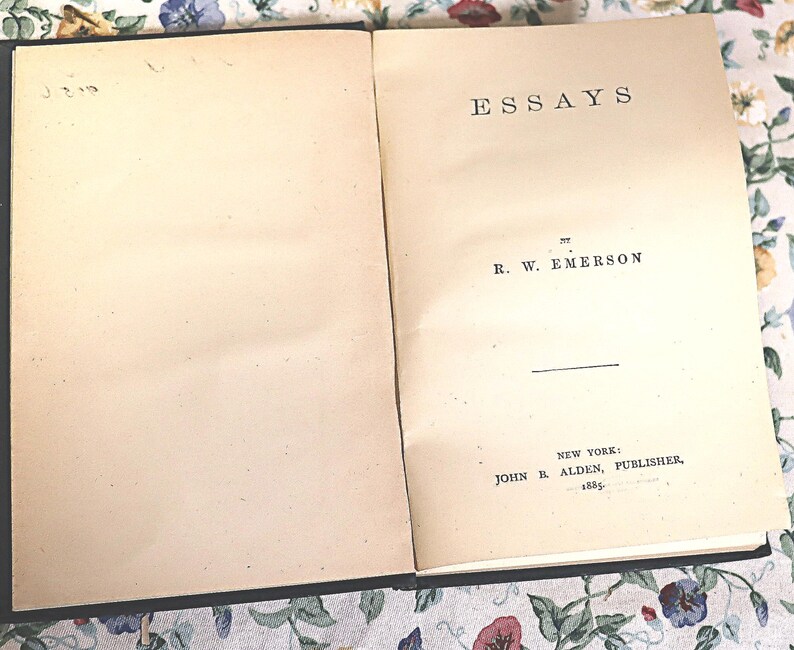 May include: Open book with the title "ESSAYS" by R. W. Emerson. The book is open to the title page, with the publisher's information at the bottom. The pages are aged with a cream color.