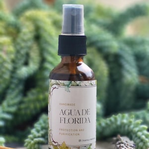 以下が含まれることがあります： 黒いキャップと「AGUA DE FLORIDA」と書かれた白いラベルが付いた、茶色のガラススプレーボトル。 ラベルには「Protection and Purification」と「Handmade」とも書かれています。 ボトルは緑とスパイスに囲まれています。