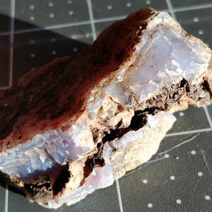 May include: A rough-hewn stone with a light blue interior and a dark brown exterior. The stone has a layered appearance, with the blue section appearing translucent. The surface is textured and irregular, with a natural, earthy aesthetic.