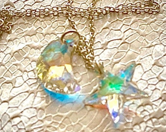 Puede incluir: Un collar de cadena plateada con un colgante de cristal en forma de media luna y una estrella de cristal. Los cristales son iridiscentes y brillan a la luz.