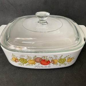 Puede incluir: Fuente de horno blanca con tapa de cristal transparente. El plato presenta un borde colorido de verduras y el texto "L'Echalote". El plato tiene asas blancas a cada lado.