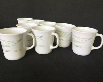May include: Set of eight white ceramic mugs with a blue and green floral design. The mugs have a rounded shape and a handle.