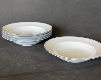 May include: Four white ceramic soup bowls with a thin blue rim. The bowls are stacked on top of each other.