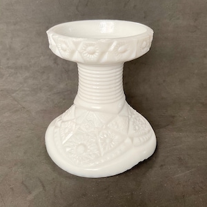 Op de afbeelding: Witte melkglazen voet met een reliëf bloemmotief. De voet heeft een brede basis en een smalle bovenkant.